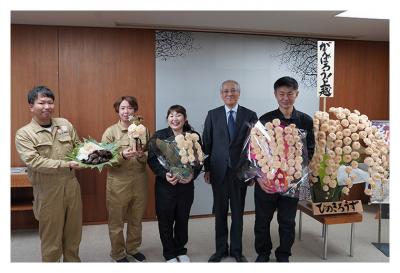 飯塚達治建設代表ほかによるヒノキのカンナ屑で作ったバラの花「ひのきろうず」と生キクラゲの栽培取組の報告（写真）