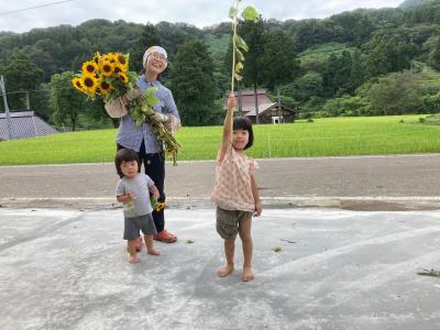 収穫した花をかかげる子どもと、笑顔の鴫谷さん（写真）