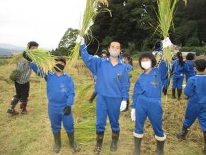 刈り取った稲を手にする小学生（写真）