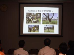 資料館内でNPO法人の活動内容について紹介を受ける会員の様子（写真）