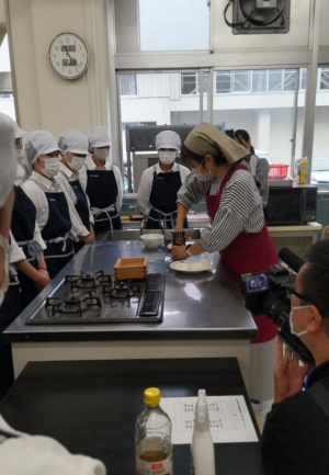 牛乳パックの中に笹寿司の具材を入れる講師（写真）