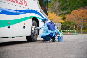 事業者がバスの右前輪を簡易除染する様子(写真)