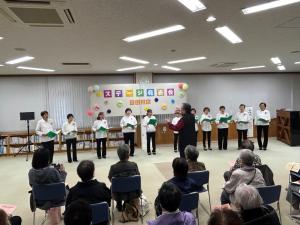 ステージで合唱を披露する団体と、鑑賞しているお客さんの様子（写真）