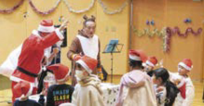 大きな袋を持ったサンタクロースとトナカイ（写真）こどもたちもサンタクロースの帽子をかぶっています