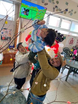 枝の高い場所にお菓子をつけようとする男の子と両親（写真）